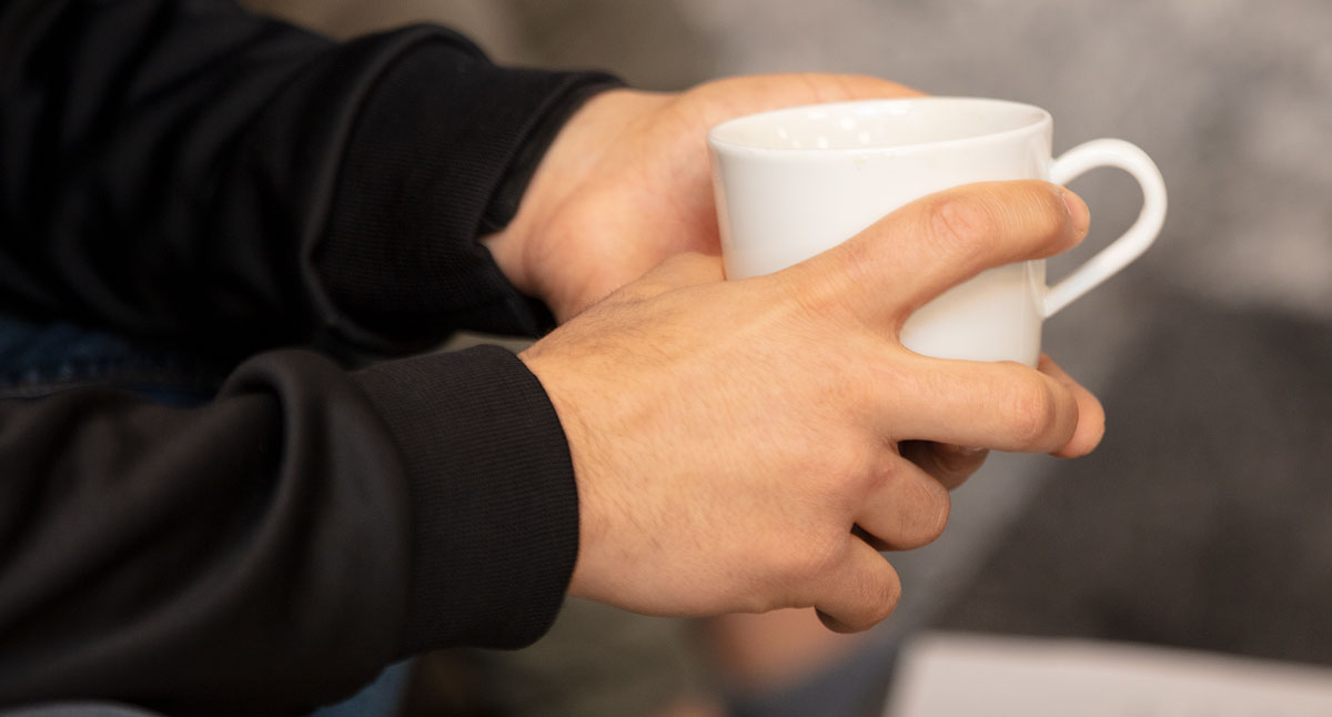 Närbild på händer som håller i en vit kaffekopp.