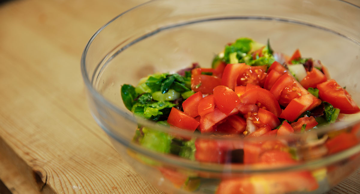 Närbild på skuren sallad och tomat i en skål av glas.